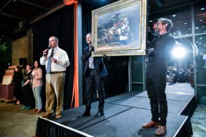 Two men holding a painting as it is being auctioned.