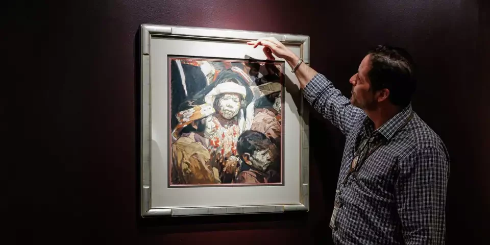 A man pointing at a painting that has many muted color tones and three faces on it.